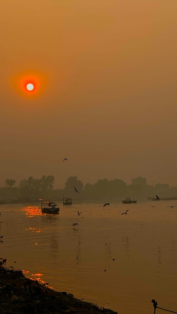 Hazy orange sunset over a river with boats and birds